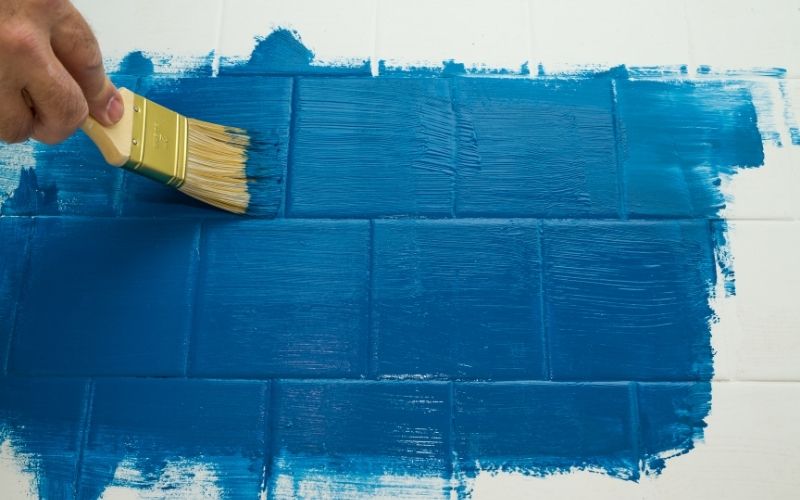 Application de peinture sur carrelage au pinceau dans un chantier de rénovation complète de salle de bain à Paris.